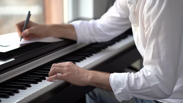 The composer plays the piano composes music and writes it down with notes alt