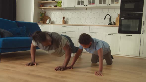 Active African American Father and Cute Son Doing Push Ups Exercise at Home alt