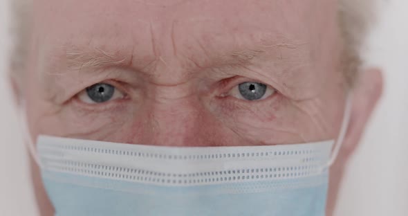 Macro Look Into Camera of Wrinkled Senior Man with Sad Blue Eyes and Mask alt