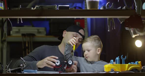 Father And Son Fixing Together A Toy Tractor With Screwdriver In Garage alt