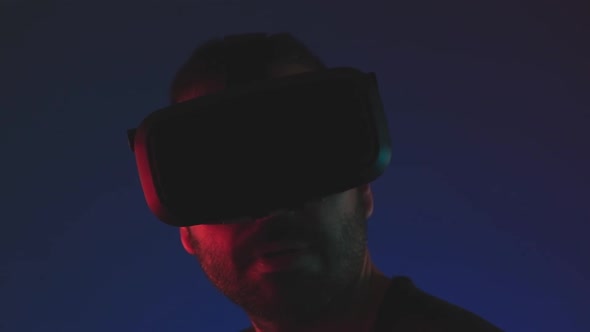 Young Man in VR Glasses Headset Interact with Virtual Reality in Color Neon Light Close Up Future alt