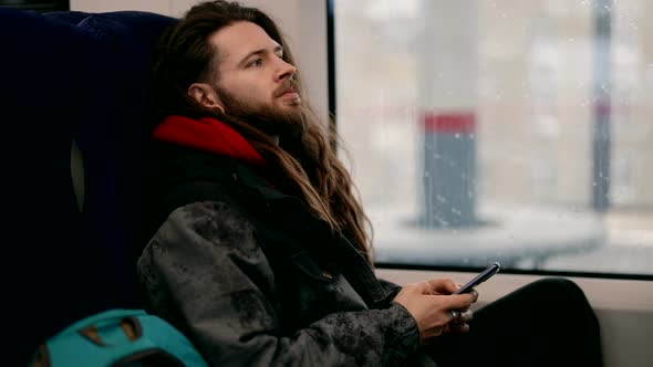 A Man with a Beard and Long Hair Who Uses a Smartphone on a Subway Train alt