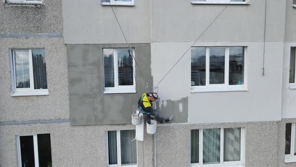 An Industrial Climber Suspended on Ropes and Paints the Wall of a Building with a Roller