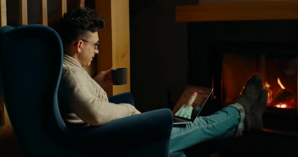Man Makes Online Video Call on Laptop and Talks with Woman at Fireplace