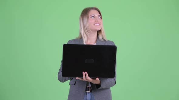 Happy Young Blonde Businesswoman Thinking While Using Laptop alt