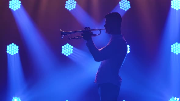 Silhouette of a Trumpet Player Performance on Stage with Blue Spotlights. Trumpet in Hands Close Up alt