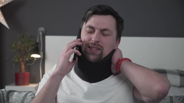 Man in Foam Cervical Collar is Calling on Phone to the Insurance Company for Medical Assistance alt