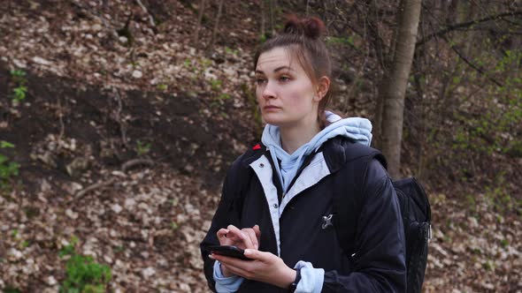 Woman with a Backpack Looking the Route on the Maps on the Phone in the Forest alt