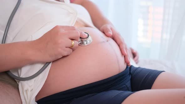 Close up husband hand touch pregnant wife belly then use stethoscope to listen to sound of baby