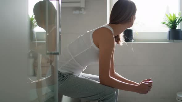 Young woman sitting on domestic bath edge and waiting for pregnancy test results. Shot with RED heli alt