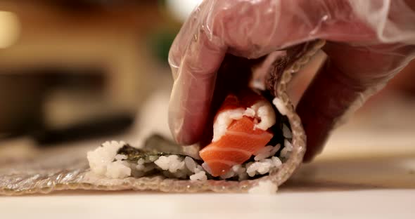 Hands Of A Sushi Chef Rolling Salmon Sushi Rolls By A Bamboo Mat In The Kitchen. Making Sushi Rolls. alt