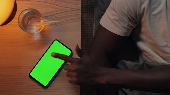 African American Man in Bed Tapping on Green Screen of Smartphone