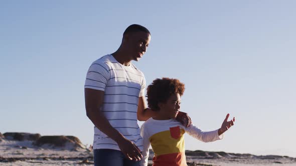 African american father and son enjoying the view while standing the beach alt