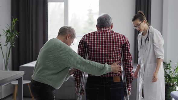 Old Man Making First Steps with Crutches at Clinic alt