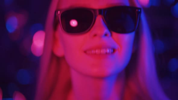 Joyful Blonde Woman in Sunglasses Actively Moves to the Loud Music of the Nightclub