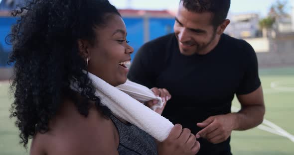 Curvy african woman talking with her personal trainer while checking tech clipboard outdoor alt