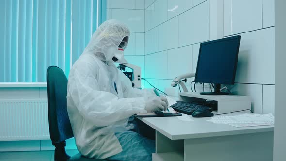 A Medic in Protection Suit and Mask Writing in Notebook in Light White Lab alt