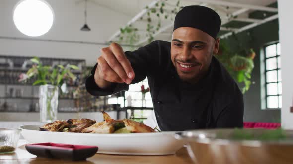 Mixed race male chef preparing a dish and smiling in a kitchen alt