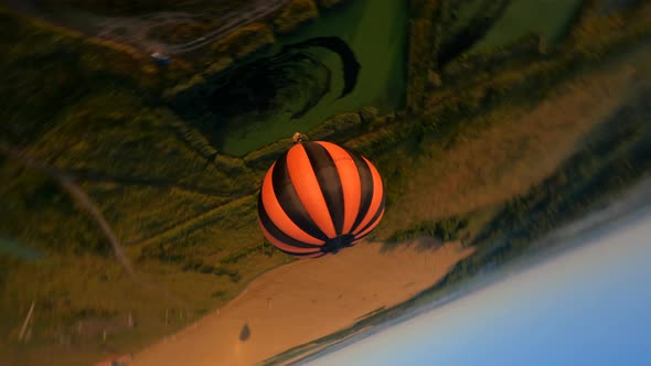 Black and orange hot air balloon floating above swamp, beautiful sunrise.