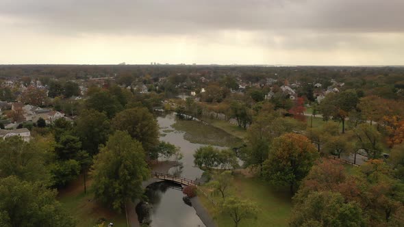 A drone shot of a long pond on a cloudy day. The camera dolly in over it as the sun shines through t alt