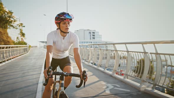 Lady in Sportswear and Protective Helmet is Riding Trekking Bike Downhill Along Bridge Surrounded By alt