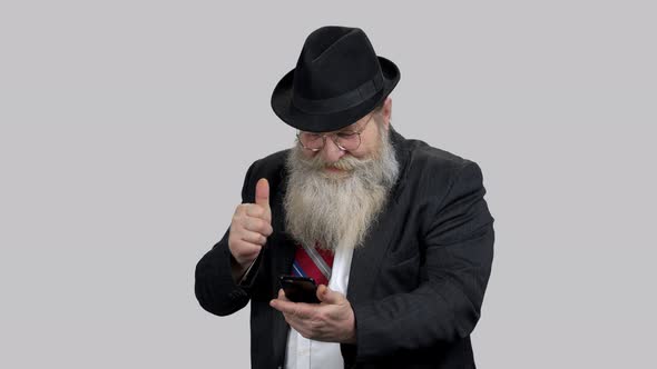 Old Happy Man Shows Thumb Up To Someone Online Using His Phone alt