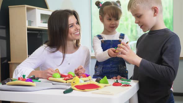 Caucasian girl and boy kid playing and learning at preschool with female teacher. Mother, daughter a