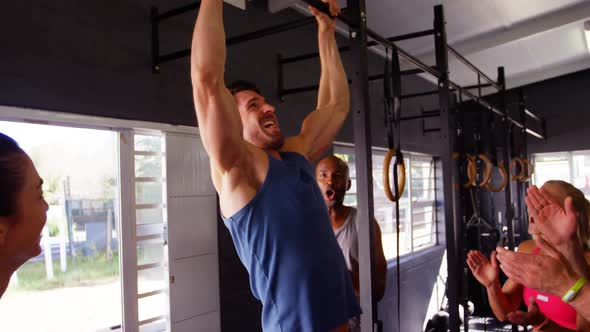 Men performing pull-up exercise while friends applauding him alt