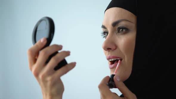 Attractive Arab Lady Applying Lip Gloss, Smiling in Mirror, Face Care, Make-Up alt