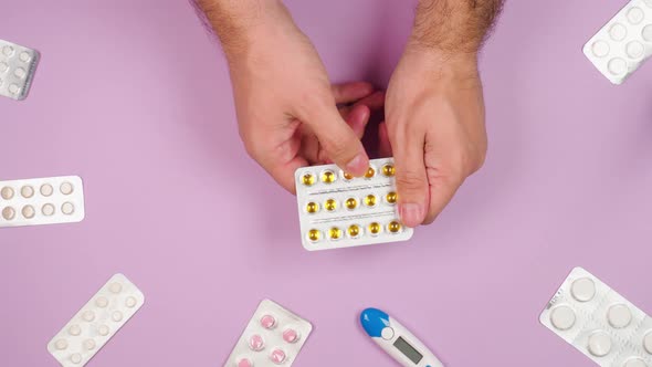 Male hands hold a blister with round yellow pills on a pink background with other medications