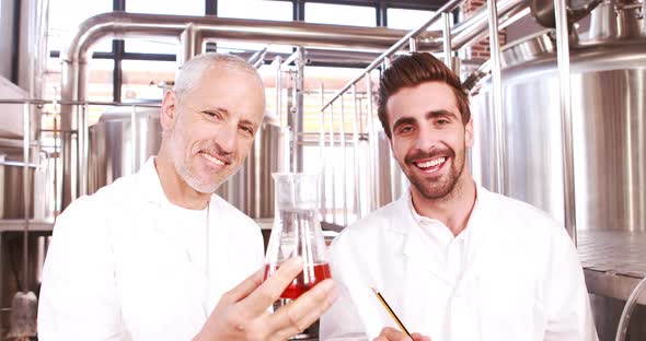 Two Men in Lab Coat Looking at the Beaker with Beer alt