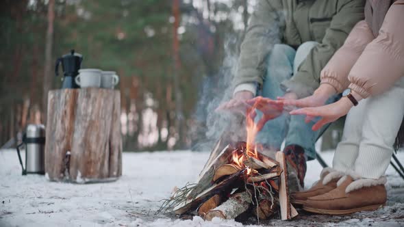 Man and Woman Warming Their Hands By a Campfire in the Woods in Winter