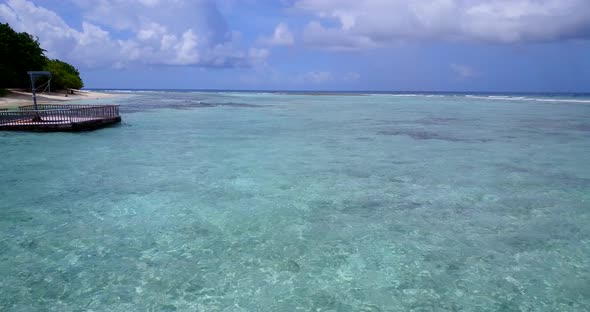 Wide birds eye tourism shot of a white sand paradise beach and aqua turquoise water background in 4K alt