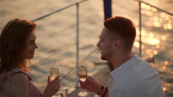 Young Happy Man and Woman Clinking with Glasses of Sparkling Wine While Yachting in Open Sea on alt