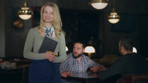 Happy Smiling Young Waitress Posing in Restaurant with Blurred Men Talking Sitting Table at alt