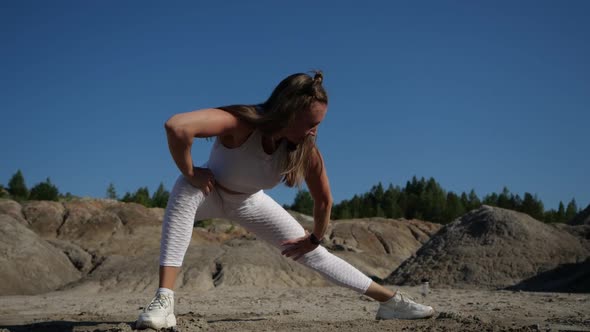 Girl Blonde in White Suit Does Stretching Legs Surrounded By Sands