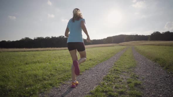 Slow Motion Following Woman Running on Gravel Road in Summer