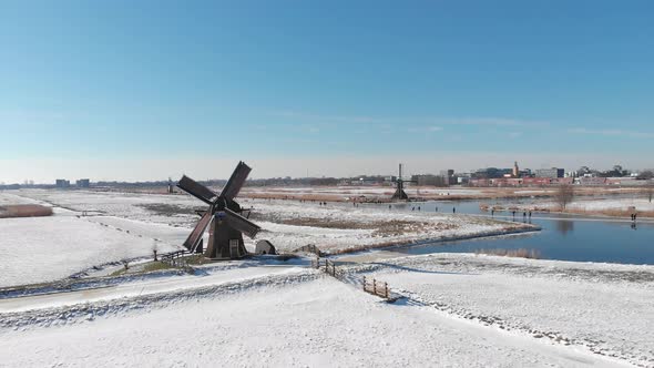 Ice skaters on frozen canal beside Netherlands windmill, winter aerial view alt