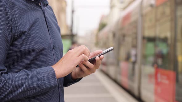 A Man Works on a Smartphone in an Urban Area  Closeup  People Get Out of a Trolley in a Street