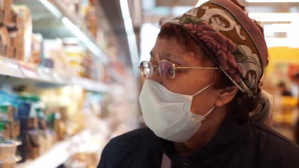 Elderly Woman in Protective Medical Mask and Medicine Gloves Choosing Products in Supermarket. The