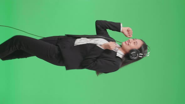 Side View Of Asian Business Woman Listening To Music With Headphones And Dancing On Green Screen alt