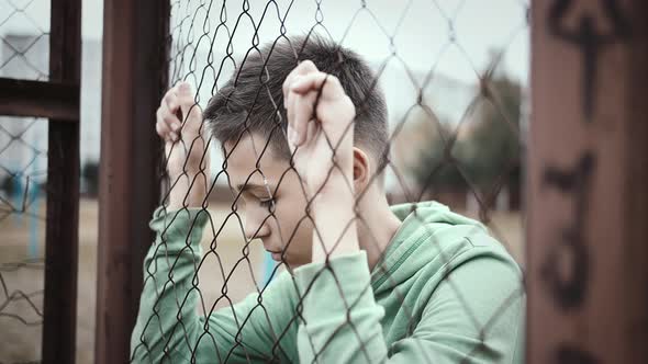 Cinematic Sad Boy Stands Alone Head Bowed Near the Fence Frustrated Boy Dropped Eyes Regrets the Act