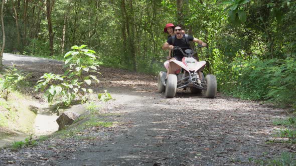 Happy young couple adventure with driving ATV travel trip on road in jungle together. alt