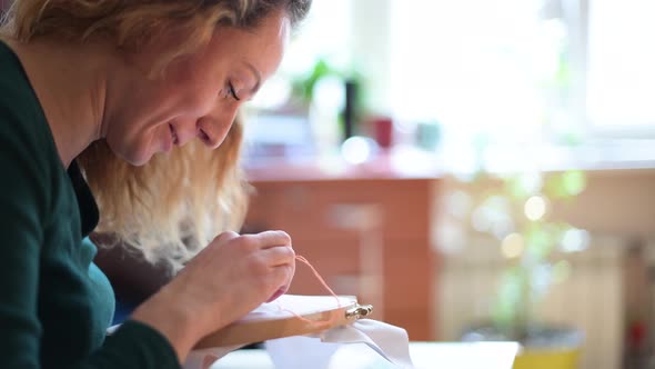Smiling and sociable girl embroiders with thread on the canvas alt