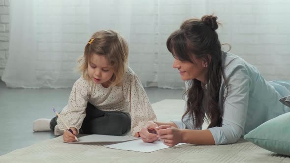 Mom and Daughter Lying on Carpet on the Floor Drawing on Paper and Having Fun alt