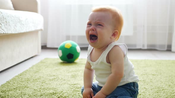 Crying Redhead Baby Girl Sitting on the Floor
