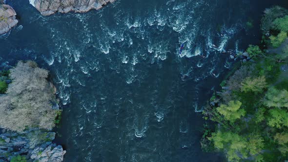 A Topdown Aerial View of a Kayak Floating on a Turbulent River Between Forest and Stone Cliffs alt