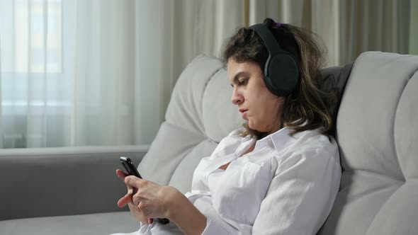 Disabled Woman in Headphones Listens to Music Holding Phone alt