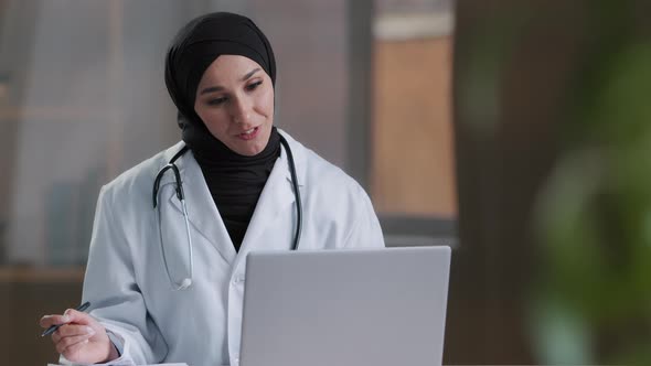 Arabian Female Therapist Doctor Wear Hijab White Coat Calling Distant Patient on Laptop Talking with alt