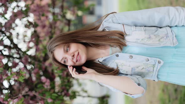 Young Model Girl Talking on the Phone Walking in the Park on a Background of Sakura Trees alt